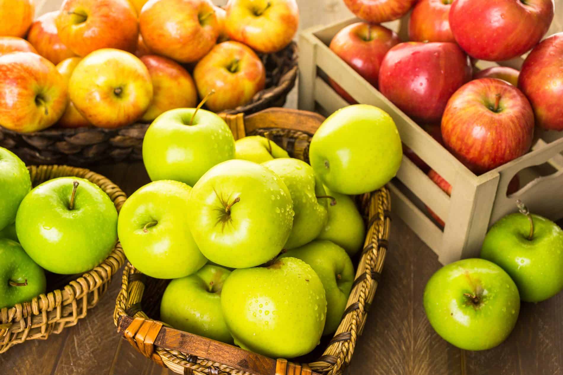 Baskets And A Crate Filled With A Variety Of Apples, Including Green And Red Ones, Arranged On A Wooden Surface.
