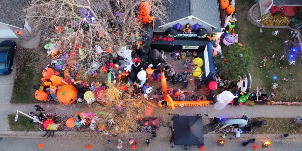 Aerial View Of A House And Yard Decorated With Numerous Colorful Halloween Inflatables, Including Pumpkins And Other Characters, Attracting Visitors On A Street.