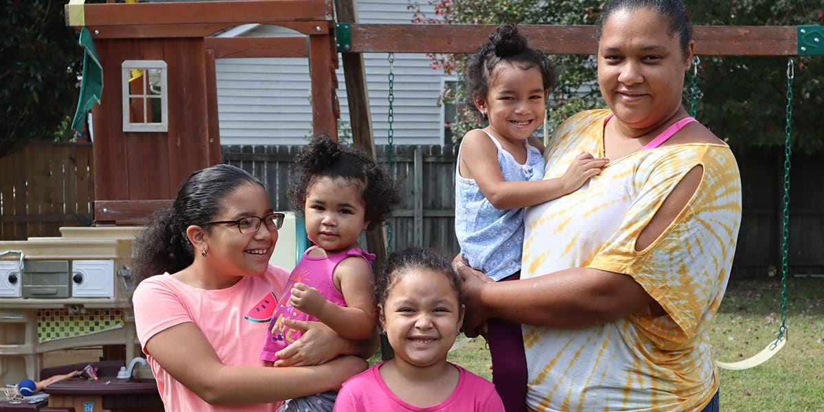 A Woman Stands Outside With Four Children, Smiling Near A Wooden Playset.