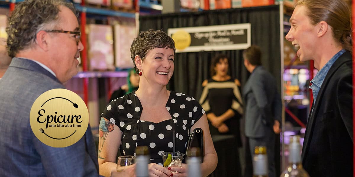 Three People Smiling And Talking At An Event With A Gold Epicure Logo In The Foreground.
