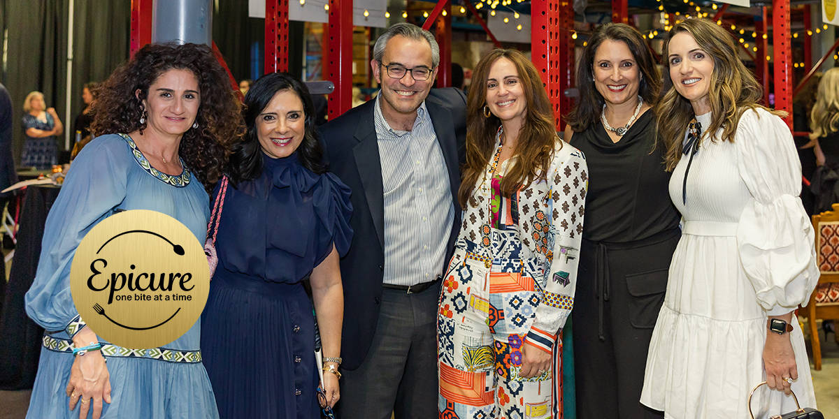 A Group Of Six People Smiling Together Indoors At An Event With An Epicure Logo In The Foreground.
