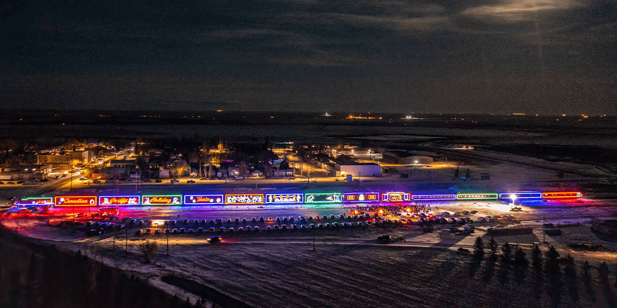 An Illuminated Train With Colorful Lights Travels Through A Snowy Landscape At Night, With A Small Town In The Background.