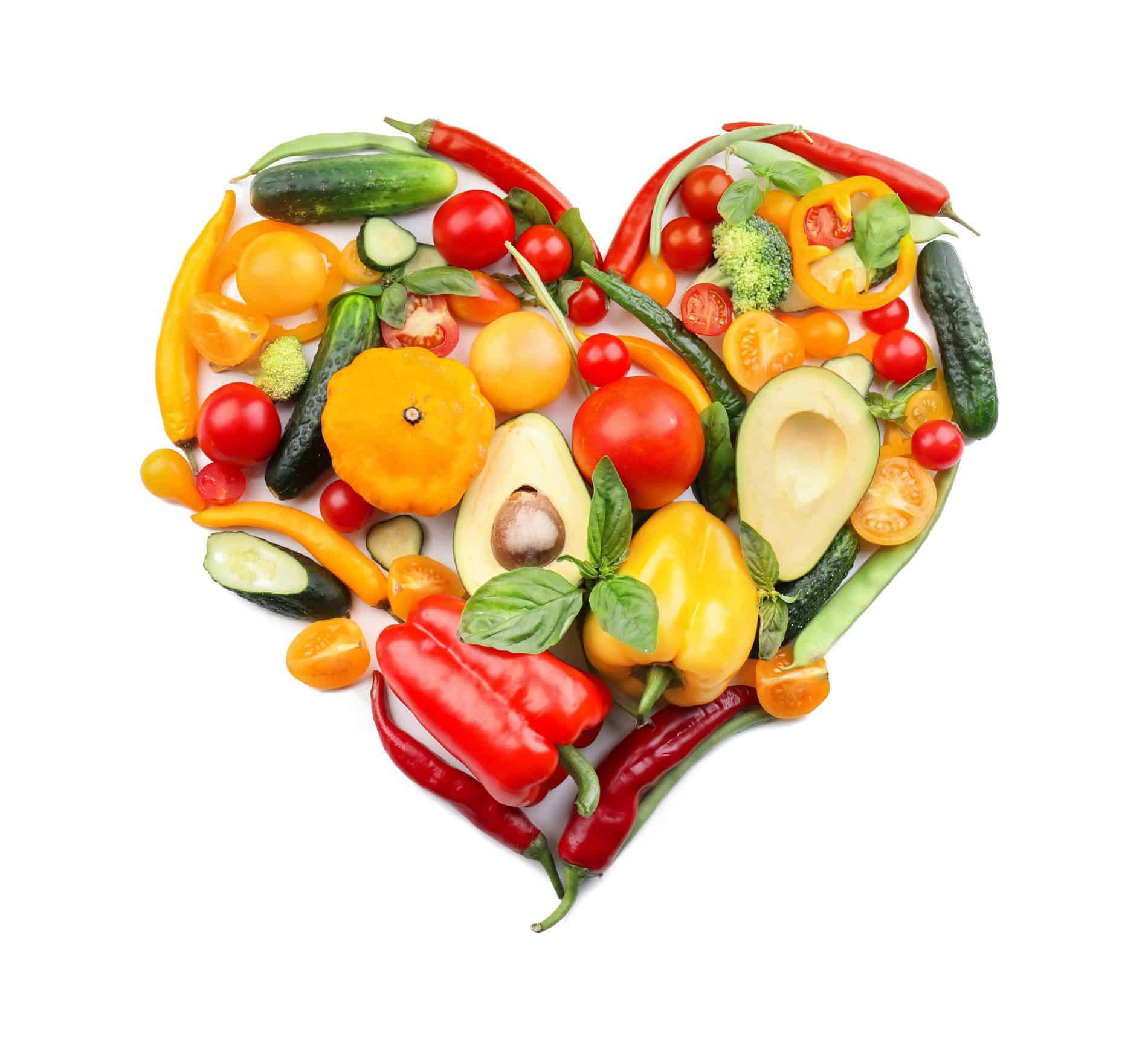 A Heart-Shaped Arrangement Of Assorted Vegetables And Fruits, Including Peppers, Tomatoes, Avocados, And Cucumbers, On A White Background.