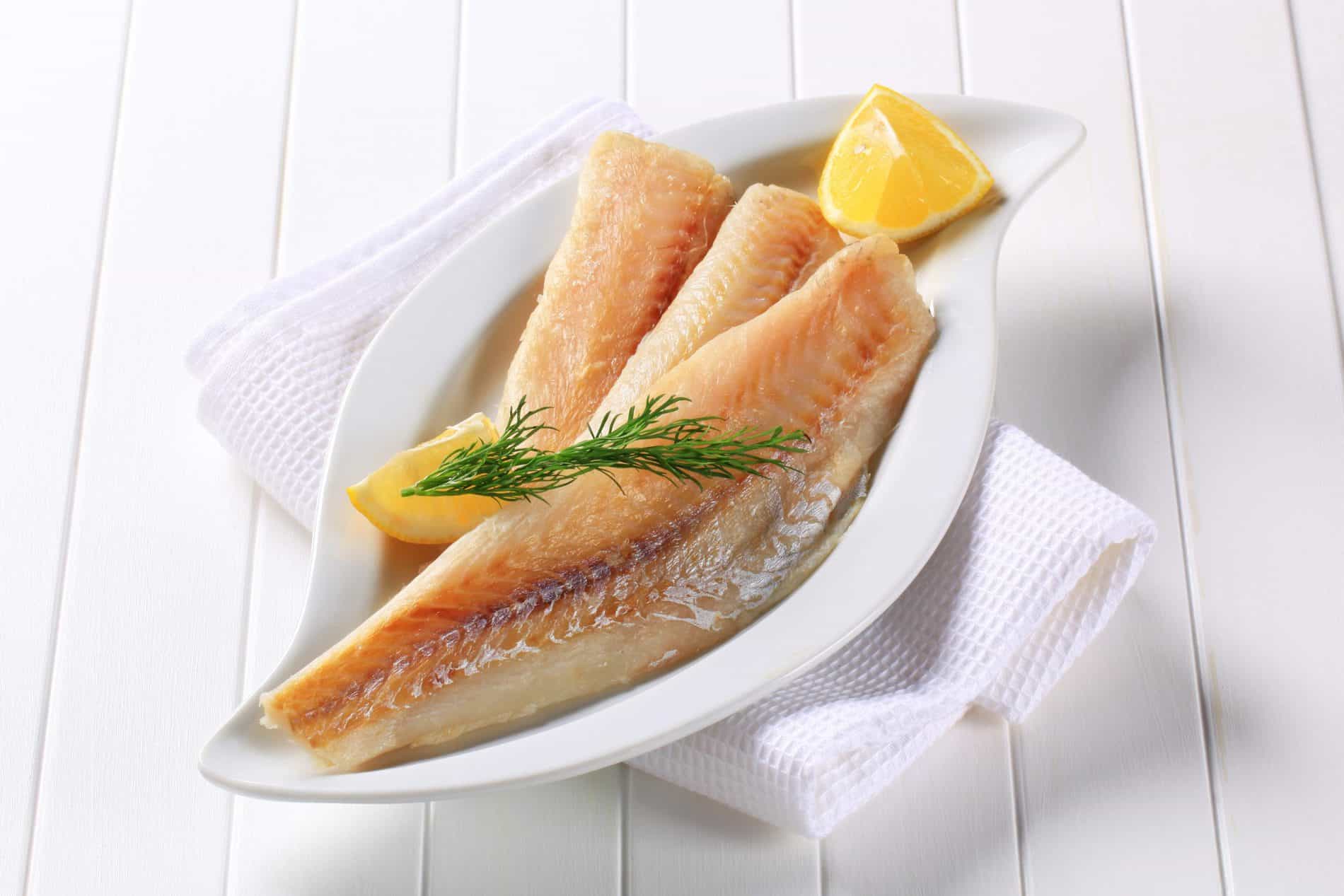Three Fish Fillets Served On A White Plate, Garnished With A Dill Sprig And Lemon Wedges.
